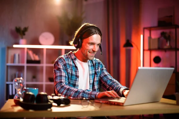 Kulaklıkla odaklanmış erkek yönetici. Bilgisayardaki video görüşmesiyle iş toplantısına öncülük ediyor. Genç adam evdeki masada otururken konuşuyor ve el kol hareketi yapıyor. Uzaktan çalışıyor.