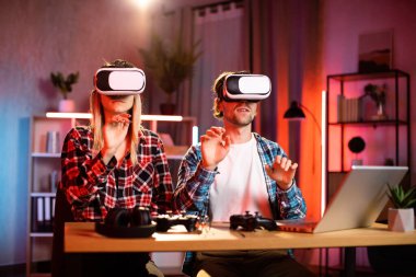 Genç, güzel bir kadın ve yakışıklı bir adam sanal gerçeklik kulaklığı takmış el ele tutuşuyorlar. Gençler evlerinde yeni moda teknolojiyle eğleniyorlar. Oyun konsepti.