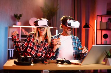 Genç, güzel bir kadın ve yakışıklı bir adam sanal gerçeklik kulaklığı takmış el ele tutuşuyorlar. Gençler evlerinde yeni moda teknolojiyle eğleniyorlar. Oyun konsepti.