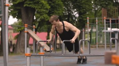 Beyaz tenli yakışıklı sporcu, açık hava konseptinde spor yaparken paralel barlarda egzersiz yapıyor..