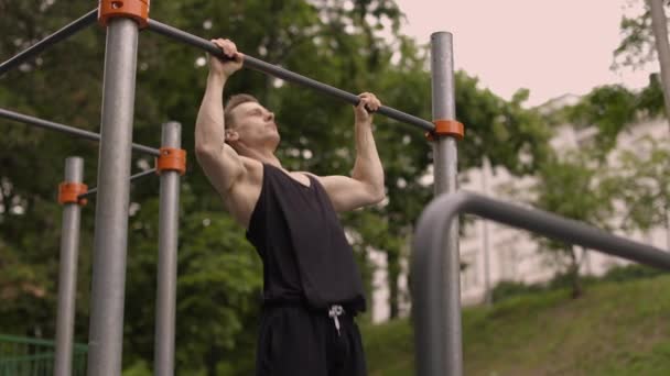 フィットネス スポーツ トレーニング ライフスタイルのコンセプト 若い男が屋外の水平バーでプルアップを行う 公園の屋外ジムで働いているスポーツマン — ストック動画