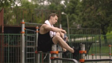 Küçük bir mola. Kaslı vücutlu genç atletik adam, sporcu ve spor modeli, paralel barlarda oturan güçlü adam. Atletik vücut şekli, adam spor salonunda rahatlıyor..