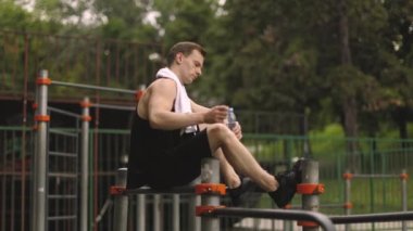 Küçük bir mola. Kaslı vücutlu genç atletik adam, sporcu ve spor modeli, paralel barlarda oturan güçlü adam. Atletik vücut şekli, adam spor salonunda rahatlıyor..