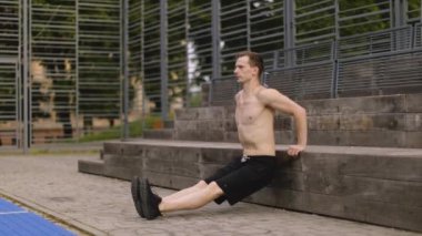 Siyah spor kıyafetleri içinde daldıran, kol kaslarını çalıştıran odaklanmış kaslı bir adamın portresi. Sportif çekici bir adam arka planda spor yapıyor ve etrafında açık bir alan yaratıyor..