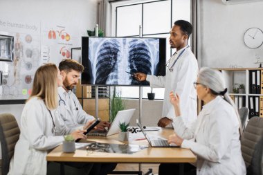 Laboratuvar önlüklü Afrikalı Amerikalı doktor uluslararası meslektaşlarıyla yaptığı konferans sırasında akciğerlerinin röntgen taramasını büyük ekranda gösteriyor. Beyin fırtınası, tıp ve işbirliği kavramı.