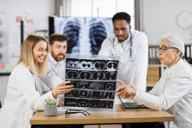 Çok ırklı erkek ve kadın doktorlar klinikte hasta X-ray taraması için brifing veriyorlar. Laboratuvar önlüklü iş arkadaşları çeşitli modern aletleri iş için kullanıyorlar..
