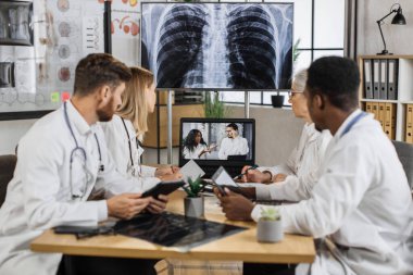 Çeşitli tıp bilim adamları, yüksek teknoloji laboratuvarında Afrika kökenli Amerikan konuşmacılarla beyin anomalileri hakkında çevrimiçi toplantı yapıyor. Nöroloji merkezinde masada otururken bilgisayar kullanan meslektaşlar.