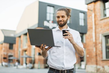 Yakışıklı beyaz adamın portresi kağıt bardakta taze içecekle ortağıyla konuşuyor internette sohbet ediyor dizüstü bilgisayarla sokakta yürüyor ve kameraya bakıyor..
