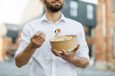 Öğle yemeğinde sebzeli salata yiyen işadamlarının yakın görüntüsü şehrin arka planında ayakta duran sağlıklı yiyecekler, yaşam tarzı konsepti tanınmayan insanlar..