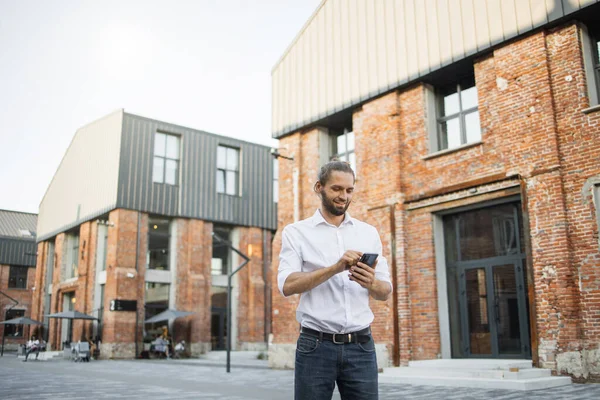 Başarılı genç bir iş adamının portresi. Beyaz tişörtlü, sarı saçlı bir adam. Eski şehir binalarının arka planına telefon ediyor..