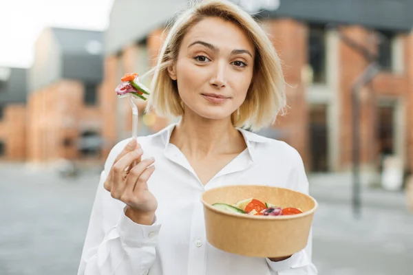 一方では段ボールのボウルに野菜サラダを保持するビジネス女性のクローズアップ肖像画と他方でキュウリとトマトのスライスとフォーク — ストック写真