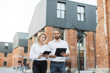 İki Kafkasyalı ofis çalışanı dışarıda birlikte yürüyüp gülümsüyor ve sohbet ediyorlar. Beyaz gömlekli yakışıklı bir adam, elinde pano ve elinde tablet tutan çekici bir kadın..