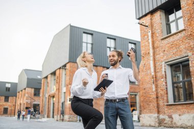 Dışarıda gülerek ve sohbet ederek yürüyen iki mutlu ofis çalışanı. Akıllı telefon ve kahve taşıyan yakışıklı bir adam. Tablet tutan çekici bir kadın..