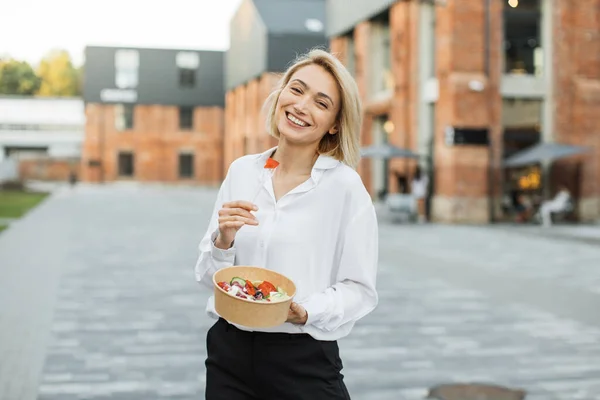 陽気なブロンド女性フリーランスの屋外夏の肖像彼女のおいしいサラダを楽しむ仕事の休憩の街の通りを歩く — ストック写真