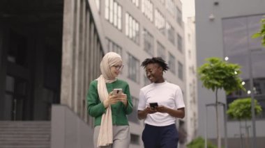 Arap iş arkadaşı, resmi yeşil giysiler içinde sokakta yürüyor ve akıllı telefon kullanan ve gülümseyen Afrikalı genç bir kadınla bazı iş konularını tartışıyor..
