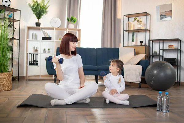 Sport, workout concept. Mom and Little Girl doing dumbbell exercises on a yoga mat in the living room at home. New normal concept. Healthy lifestyle. Relaxing at home.