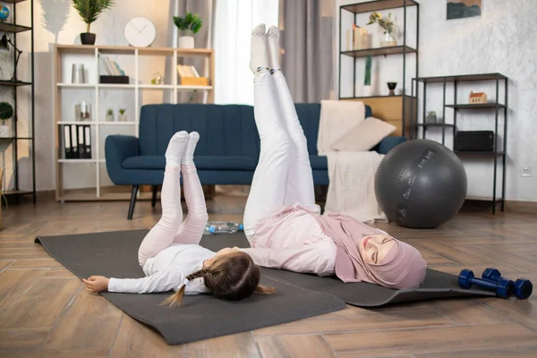 Muslim mom and little girl exercise stretching muscles together at home. Recreation workout with mother and charming daughter leg stretching warm-up ready to exercise.Family Sporty Concept