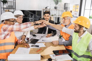 Mutlu çok ırklı mimarlar, mühendisler ve tasarımcılar toplantı odasında başarılı bir şekilde el ele tutuşuyorlar. Mimari proje toplantısına erkek ve kadın meslektaşlar liderlik ediyor.