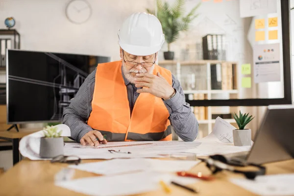 Architect mature man or male builder hold pen and ruler, writing and drawing architectural project, work on laptop computer on the desk at workplace.