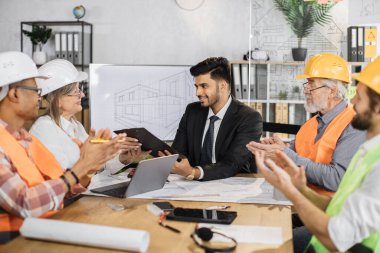 Hintli işadamı, bir inşaat şirketinin kıdemli patronunun sözleşmesini ve belgelerini imzaladı. Çeşitli mimarlar, tasarımcılar ve mühendisler modern cihazlar ve planlarla masada oturuyorlar.