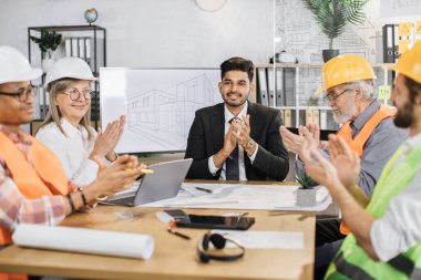 Yeni projenin sunumu sırasında ofiste oturup alkışlayan mutlu inşaat ekibi. İş hayatında başarı. Uluslararası işbirliği.