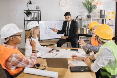 Ofiste projelerle çalışan beş çok ırklı ortak büyük dijital ekranın yanında oturuyor. Profesyonel inşaat ekibi yeni binada servis hatlarının düzenlenmesini tartışıyor.