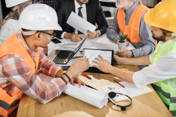 Construction team analysing blueprints during business meeting at office . Multiracial partners using digital tablet for work. Concept of cooperation and brainstorming.