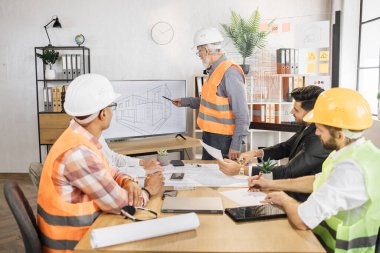 Beş uluslararası ortaktan oluşan bir grup, ev çizimiyle etkileşimli dijital ekrana bakarak yeni binanın tasarımı ve ölçümlerini tartışmak üzere çalışma toplantısı yapıyorlar. Takım çalışması, beyin fırtınası konsepti