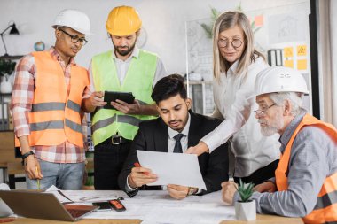 Yaratıcı tasarımcılar, mimarlar ve mühendisler yeni inşaat projesini planlamak için modern ofiste toplandılar. Birlikte çalışan beş farklı etnik gruptan oluşan bir grup..