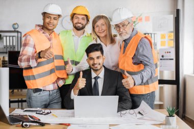 Nitelikli mimarlardan, mühendislerden ve tasarımcılardan oluşan bir ekip, ofis içinde toplantı yapıyor, Hintli bir patronun yanında duruyor, dizüstü bilgisayarla masaya oturuyor, kameraya bakıyor..