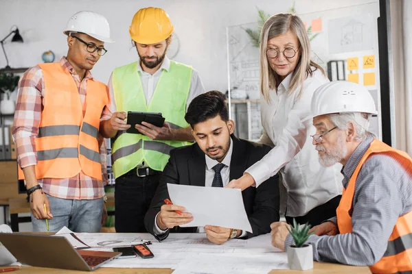 Creative designers, architects and engineers gathering at modern office for planning new construction project. Group of five multi ethnic people cooperating together.