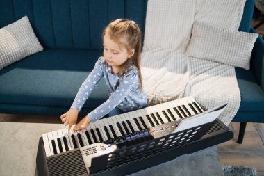 Küçük tatlı kız müzik okulunda piyano dersi alıyor. Gülümseyen küçük kız kanepede oturuyor ve sınıfta piyano çalmayı öğreniyor..