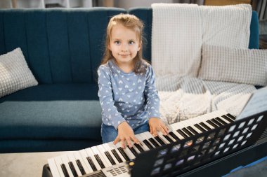 Küçük tatlı kız müzik okulunda piyano dersi alıyor. Gülümseyen küçük kız kanepede oturuyor ve sınıfta piyano çalmayı öğreniyor..