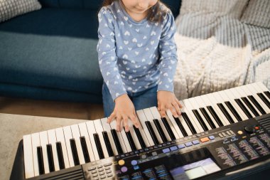 Küçük dişi ve piyano tuşlarının ellerini kapat. Güzel kız evde klasik dijital piyano çalmayı öğreniyor. Küçük çocuk anaokulu öğrencisi müzik aleti çalıyor..