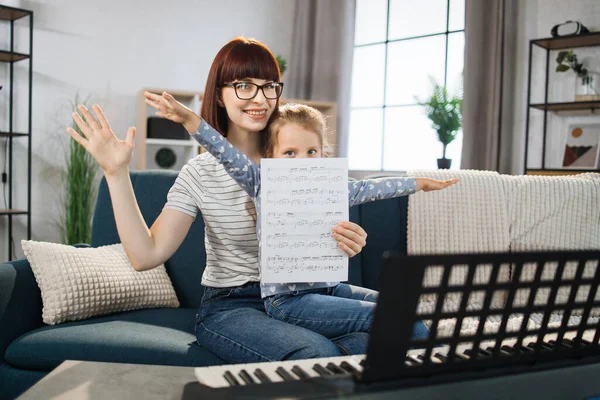 Mother teaching playing piano using notes her daughter. Little girl learning piano at home. Close up. Music class at home. Child learning piano from her mom.