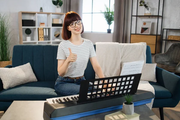 A music teacher conducts a lesson on playing a musical instrument over the Internet showing thumb up. Piano lessons online and online music training during quarantine for the coronavirus pandemic.