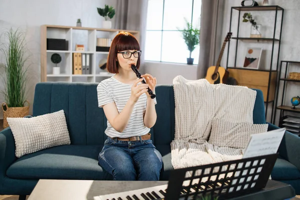 Portrait of young female playing on flute. Pretty girl learning to play classic flute at home. Beautiful student woman playing musical instrument.