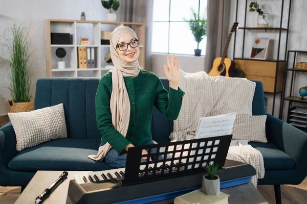 Portrait of muslim girl in hijab playing piano. Pretty women in music therapy by playing piano on music room. Young arab female girl in piano lesson. Relaxing at home waving hand. Music concept.