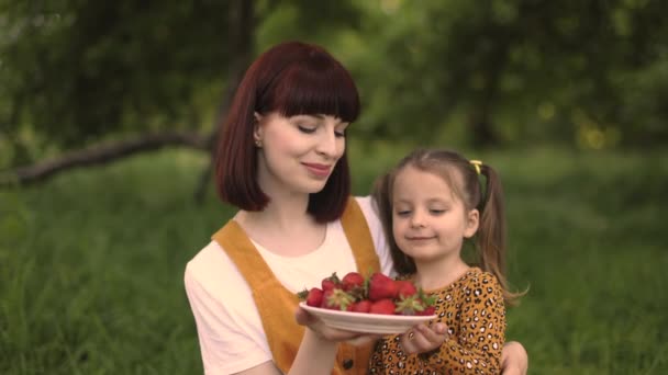 夏天的时候两个快乐的家庭 妈妈和她的小女孩在城市公园野餐 有趣的高加索妈妈和女儿在野餐时吃草莓 — 图库视频影像