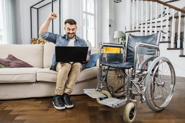 Homem Deficiente Sentado Sofá Confortável Perto Cadeira Rodas Com Laptop — Fotografia de Stock