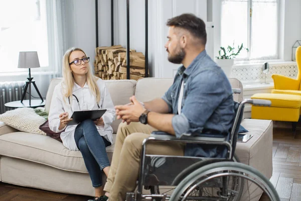 Zorgvuldige Vrouwelijke Arts Met Medische Documenten Consulteren Gehandicapte Man Woonkamer — Stockfoto