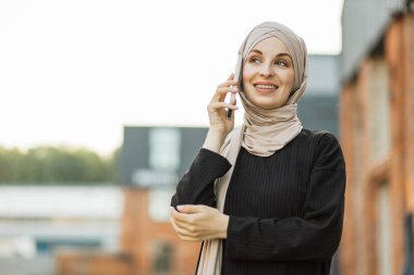 Şehir caddesinde yürürken cep telefonuyla konuşan neşeli, genç bir İslamcı iş kadını. Başörtüsü olan güzel genç bir kadın teneffüste akıllı telefon kullanıyor..