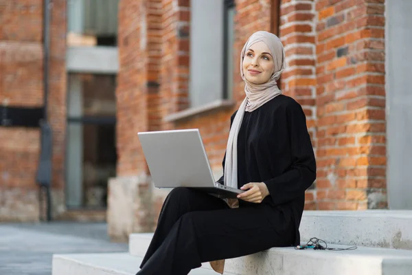 彼女のオフィスの近くに座っている間 ラップトップで働いている陽気な若いイスラム教徒の実業家 美しいです若いです女性とともにHijab作業中にラップトップを使用して休憩 — ストック写真