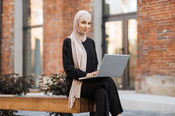 히잡을 의자에 비디오 채팅을 노트북을 사용하는 현란하게 미소짓는 사업계의 여성이다 — 스톡 사진