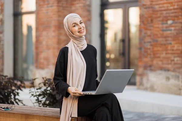 히잡에서 일하는 이슬람 프리랜서의 사진을 벤치에 노트북으로 일하고 있습니다 날씬하며 — 스톡 사진