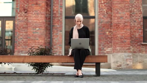 Χαρούμενη Νεαρή Ισλαμίστρια Επιχειρηματίας Που Εργάζεται Φορητό Υπολογιστή Ενώ Κάθεται — Αρχείο Βίντεο
