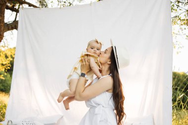 Beyaz çadırın yanında otururken güzel küçük kızını öpen ve kucaklayan mutlu beyaz bir anne. Ebeveynlik kavramı, eğlence ve boş zaman.