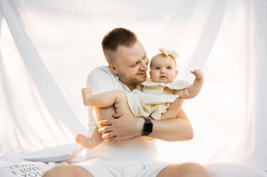 Piknik sırasında beyaz bir battaniyenin üzerinde oturmuş küçük kızı tutarken gülümseyen ve kızına bakan genç adamın portresini yakından çek. Babam sevgi dolu çocuğuyla geçirdiği her anın tadını çıkarıyor..