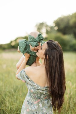 Annenin kızını elinde tutarken, çayırda yürürken görüntüsü. Küçük kız ve genç anne oyun oynuyor, birlikte vakit geçiriyorlar. Yazın dışarı çık. Dikkatsizlik bir annelik oyunudur..