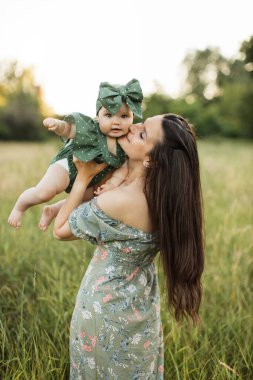 Yeşil elbiseli, muhteşem, uzun saçlı kadının arkasından manzara. Kızıyla birlikte sahada piknik yapıyorlar. Doğada annesiyle vakit geçiren güzel bir kızın açık hava portresi..